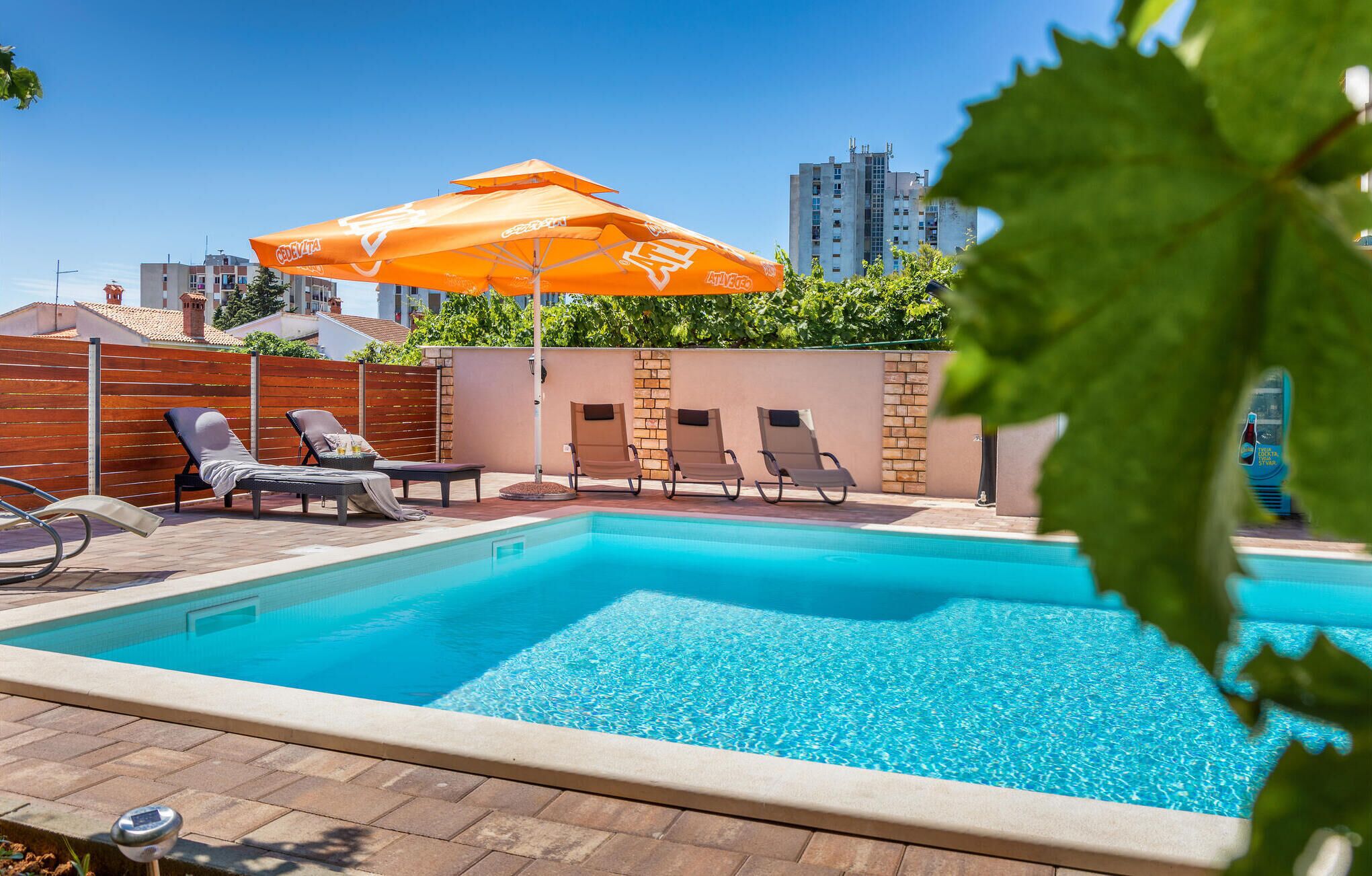Une piscine avec des chaises longues et un parasol orange.