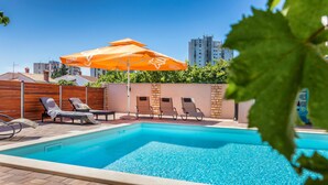 Una piscina con lettini e un ombrellone arancione.