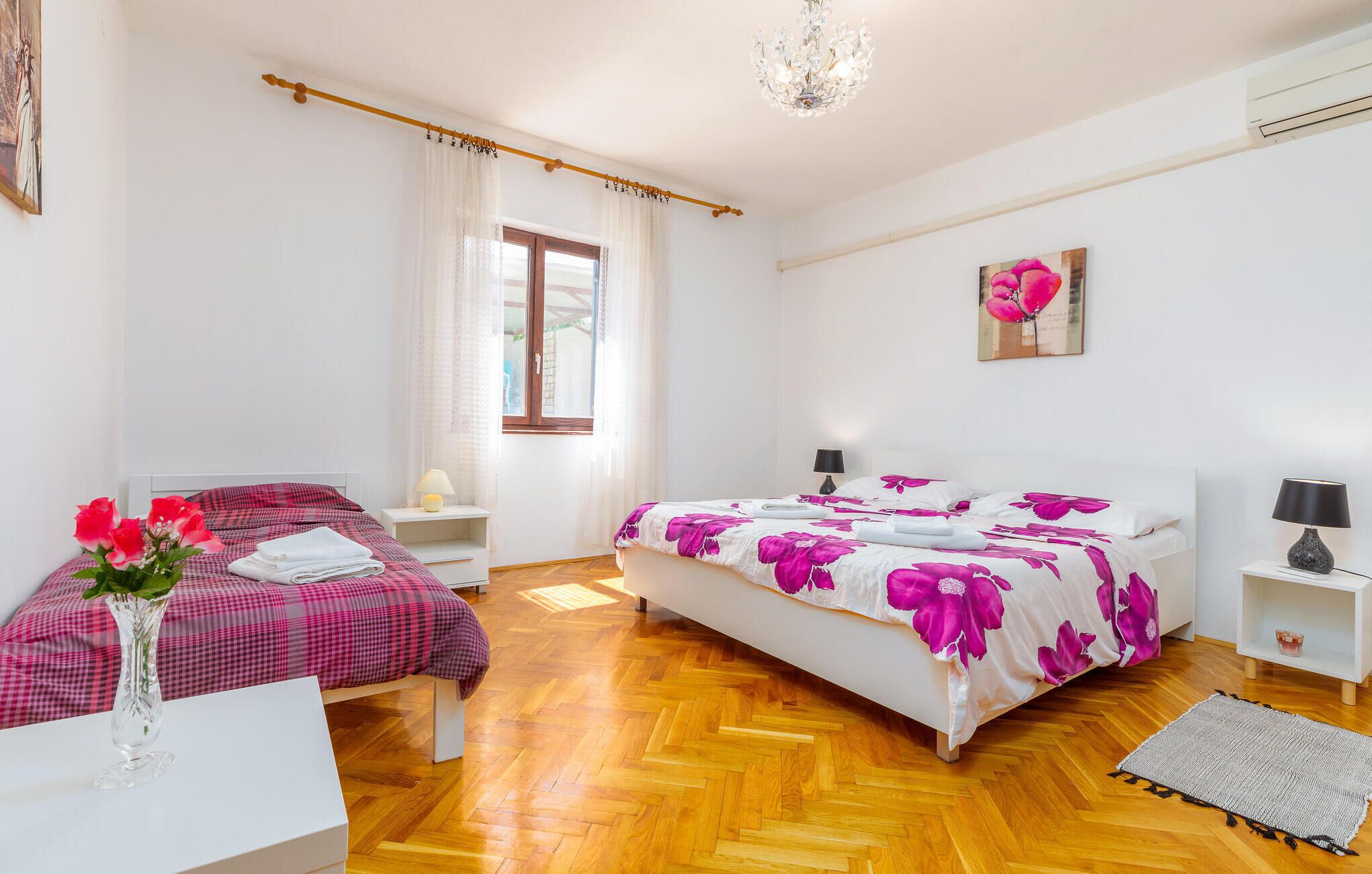 Une chambre avec deux lits, une fenêtre, un lustre et un tableau au mur.