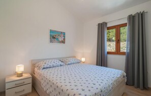 Un dormitori amb un llit, taules de nit, un quadre i una finestra amb cortines.