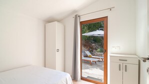 A bedroom with a bed, a wardrobe, and a sliding glass door leading to an outdoor area with a table, chairs, and an umbrella.