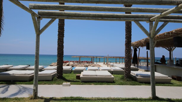 A beachside lounge area with thatched-roof structures, lounge chairs, and a view of the sea. - LOST AT SEA (Damour)