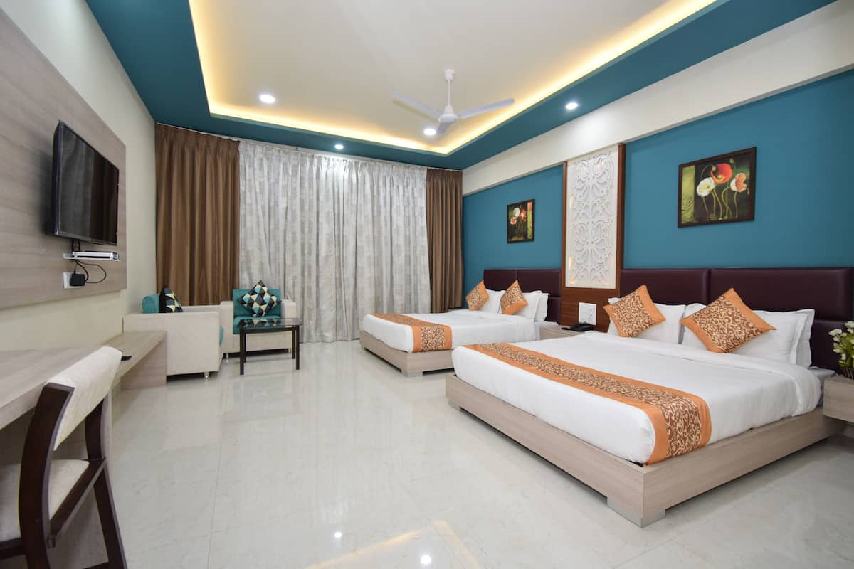Quarto de hotel com duas camas, uma escrivaninha, uma cadeira, uma televisão e um ventilador de teto.