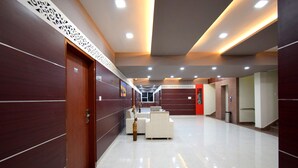 A modern hotel lobby with a long corridor, wooden paneling on the walls, and a reception desk with seating. - The Sky Imperial  Hotel Gopal Darshan (Nathdwara)