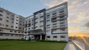 A modern multi-story hotel with a central courtyard, a covered entrance, and a view of the sunset. - The Sky Imperial  Hotel Gopal Darshan (Nathdwara)