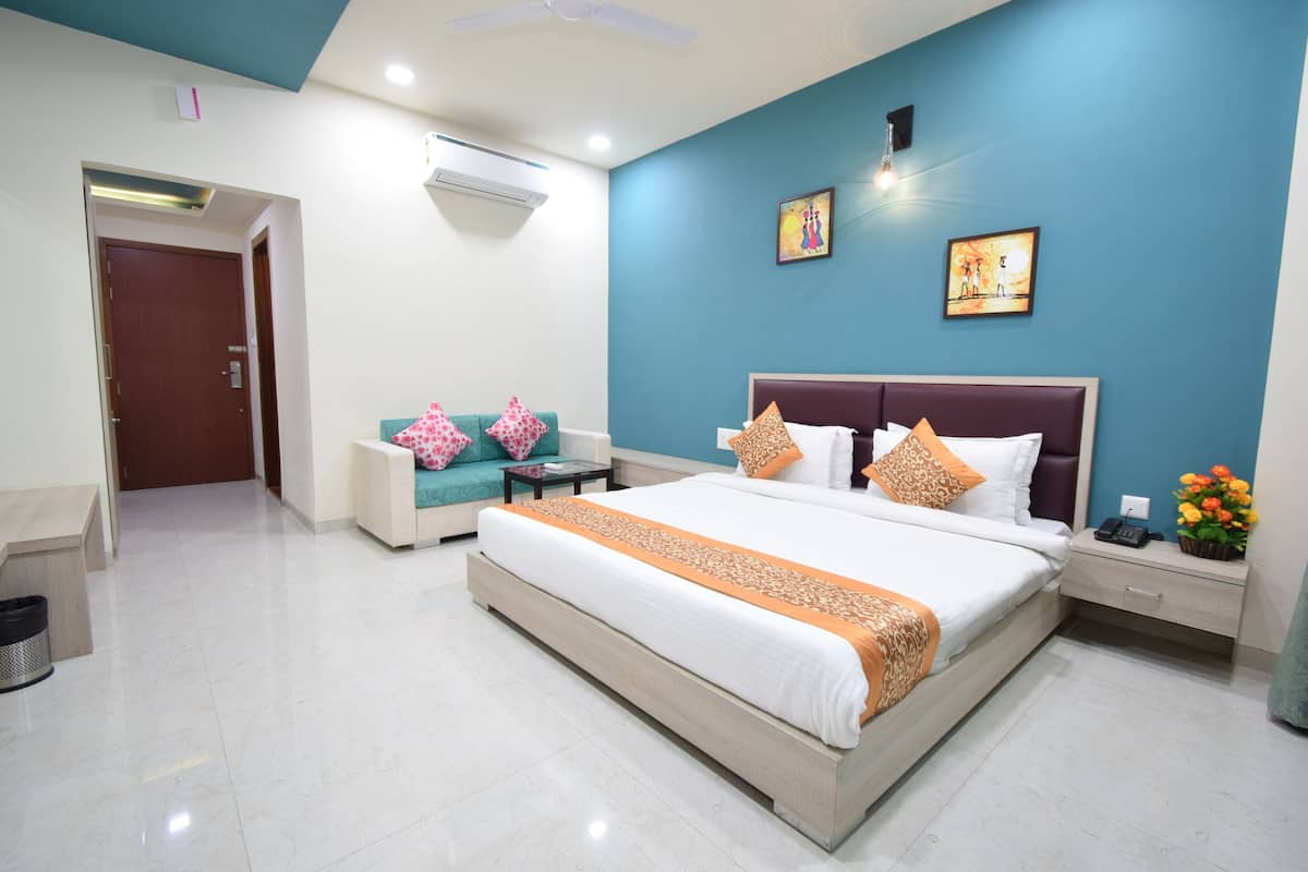 Quarto de hotel moderno com uma cama grande, um sofá, uma mesa de cabeceira e um ar condicionado fixado na parede.