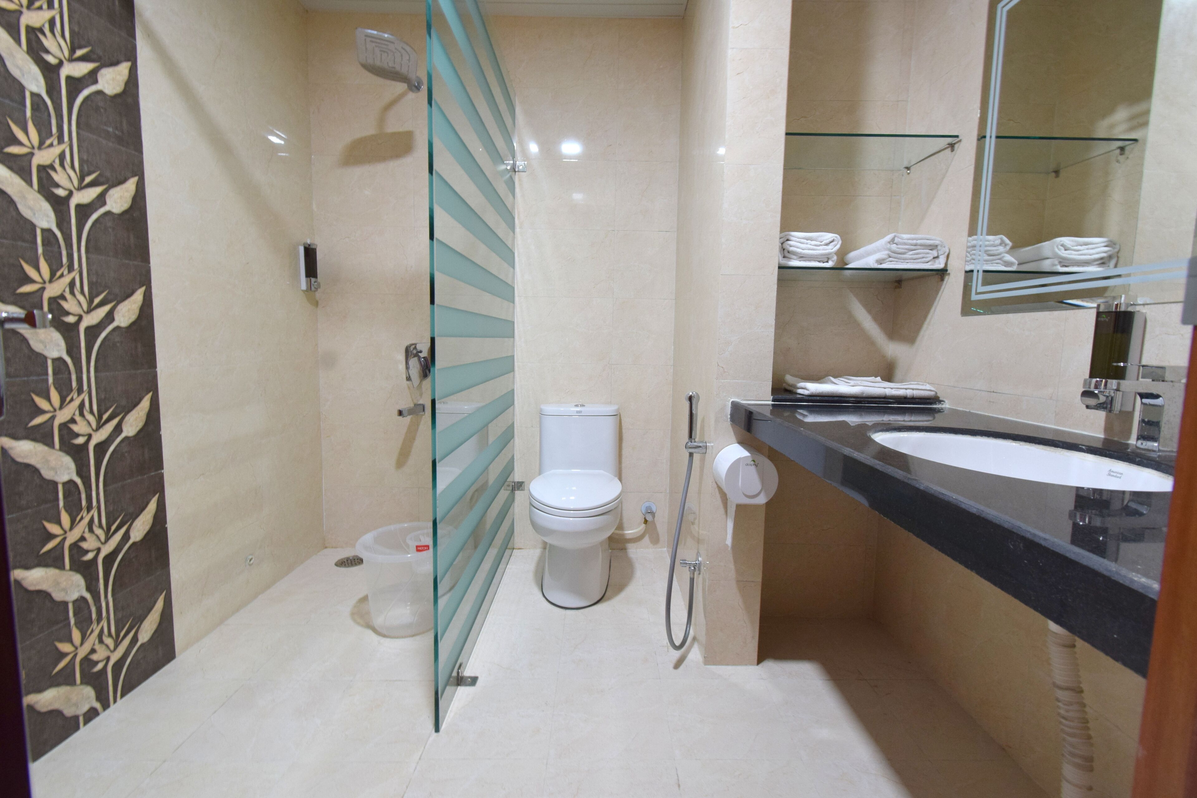 Une salle de bain moderne avec une douche à parois de verre, des toilettes, un lavabo doté d’un plan de travail noir et un miroir au-dessus du lavabo.