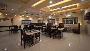 A spacious restaurant with multiple dining areas, ceiling lights, and large windows. - The Sky Imperial  Hotel Gopal Darshan (Nathdwara)