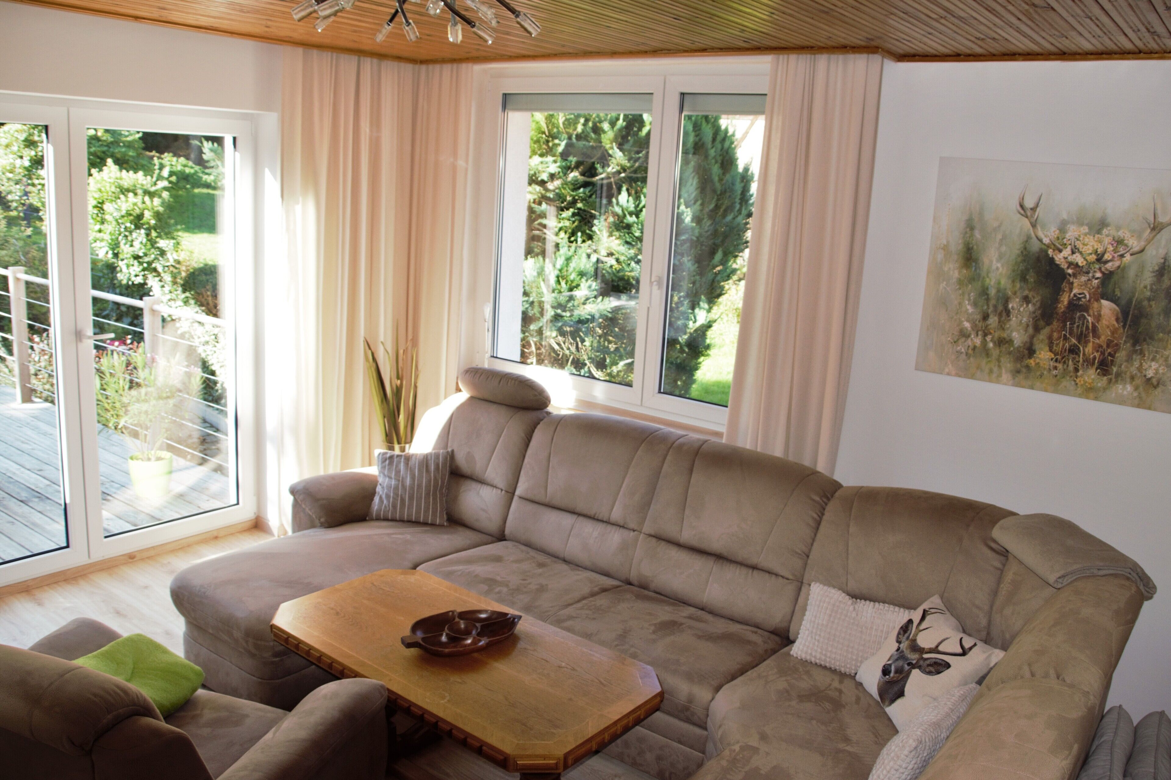 A living room with a beige sofa, a wooden coffee table, and a painting of a deer on the wall.