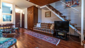 Un salon chaleureux avec un escalier en bois, un canapé à carreaux, une télévision et une grande fenêtre.