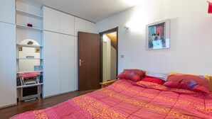 Une chambre à coucher avec un grand lit, une armoire, une télévision et une porte donnant sur une autre pièce.