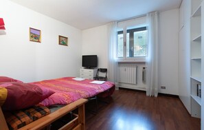 Een slaapkamer met een bed, een televisie, een stoel en een raam.