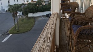 Un balcon avec des meubles en osier, une vue sur un parking et, au loin, un immeuble avec un toit bleu.