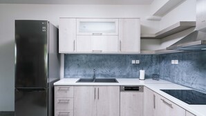 A modern kitchen with a stainless steel refrigerator, white cabinetry, a marble backsplash, and a black induction cooktop.