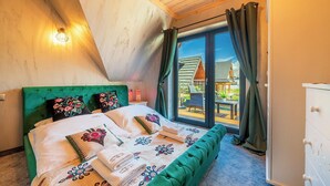 Ett sovrum med en grön klädd säng, ett träpanelat tak och utsikt över ett hus genom en glasdörr.
