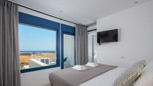 Un dormitorio con un ventanal grande, una cama con toallas ordenadas y un televisor montado.