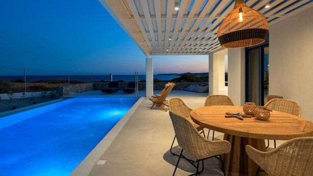 Un área de comedor moderna al aire libre con piscina, mobiliario de mimbre y vistas al océano.