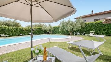 Un espace aménagé au bord de la piscine, avec des chaises longues, une table ornée d’un vase de fleurs et d’une bouteille, et un grand parasol.
