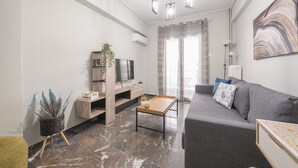 Un salon moderne avec un canapé gris, une table basse en bois, un téléviseur posé sur un meuble en bois et un grand tableau abstrait accroché au mur.