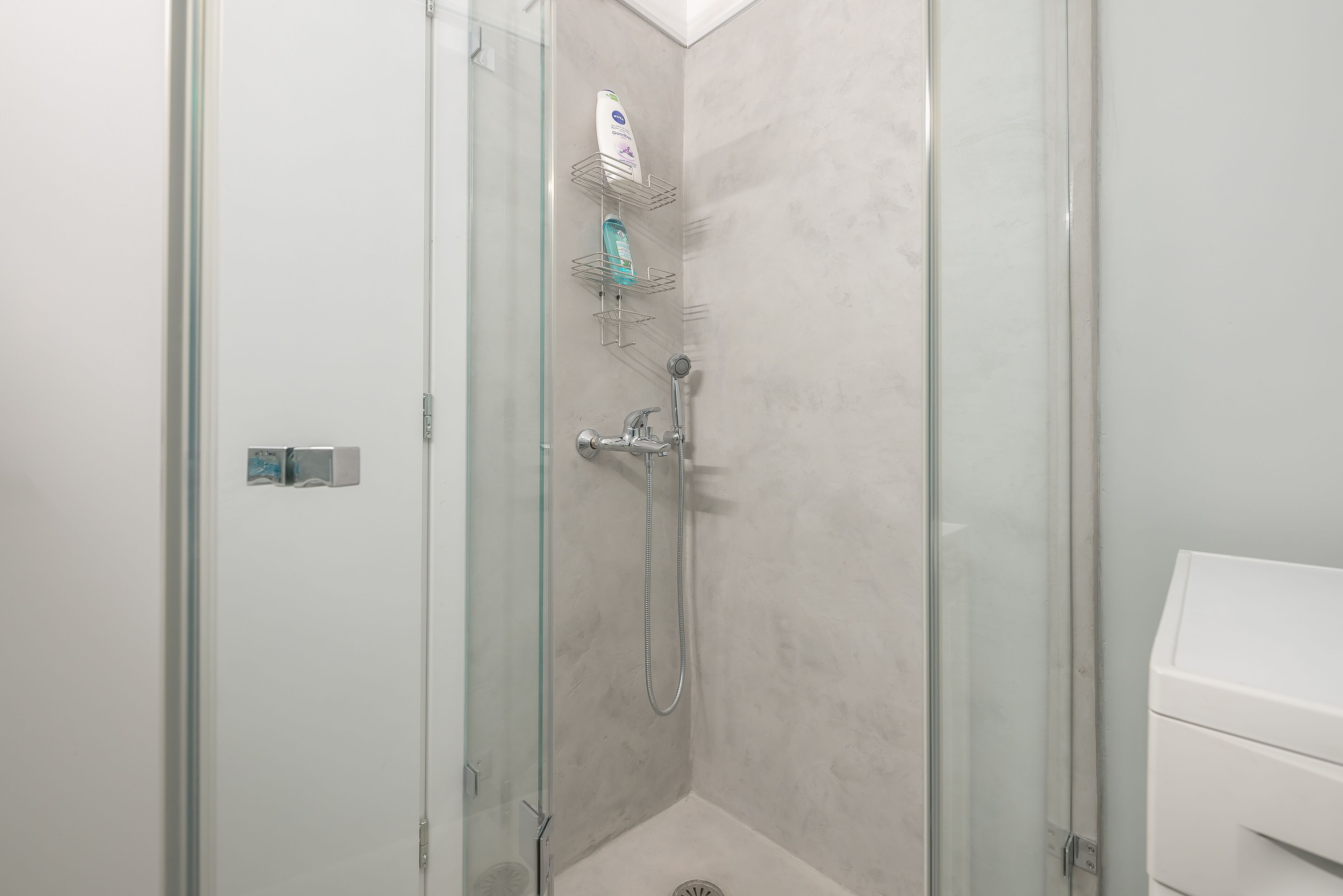 A glass-enclosed shower with a handheld showerhead and a wall-mounted faucet.