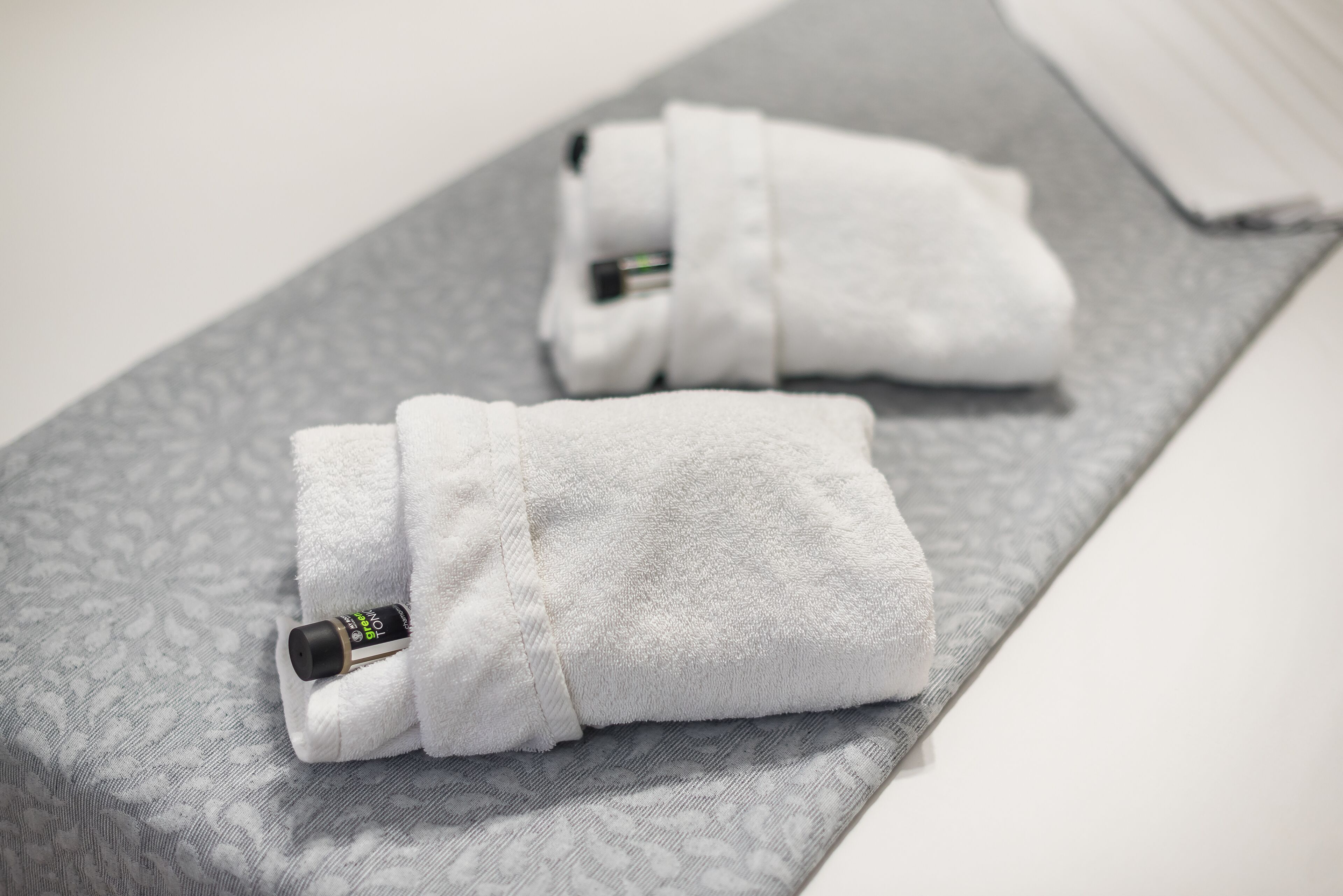 Two rolled-up towels with a black object in one of them, placed on a grey patterned mat.