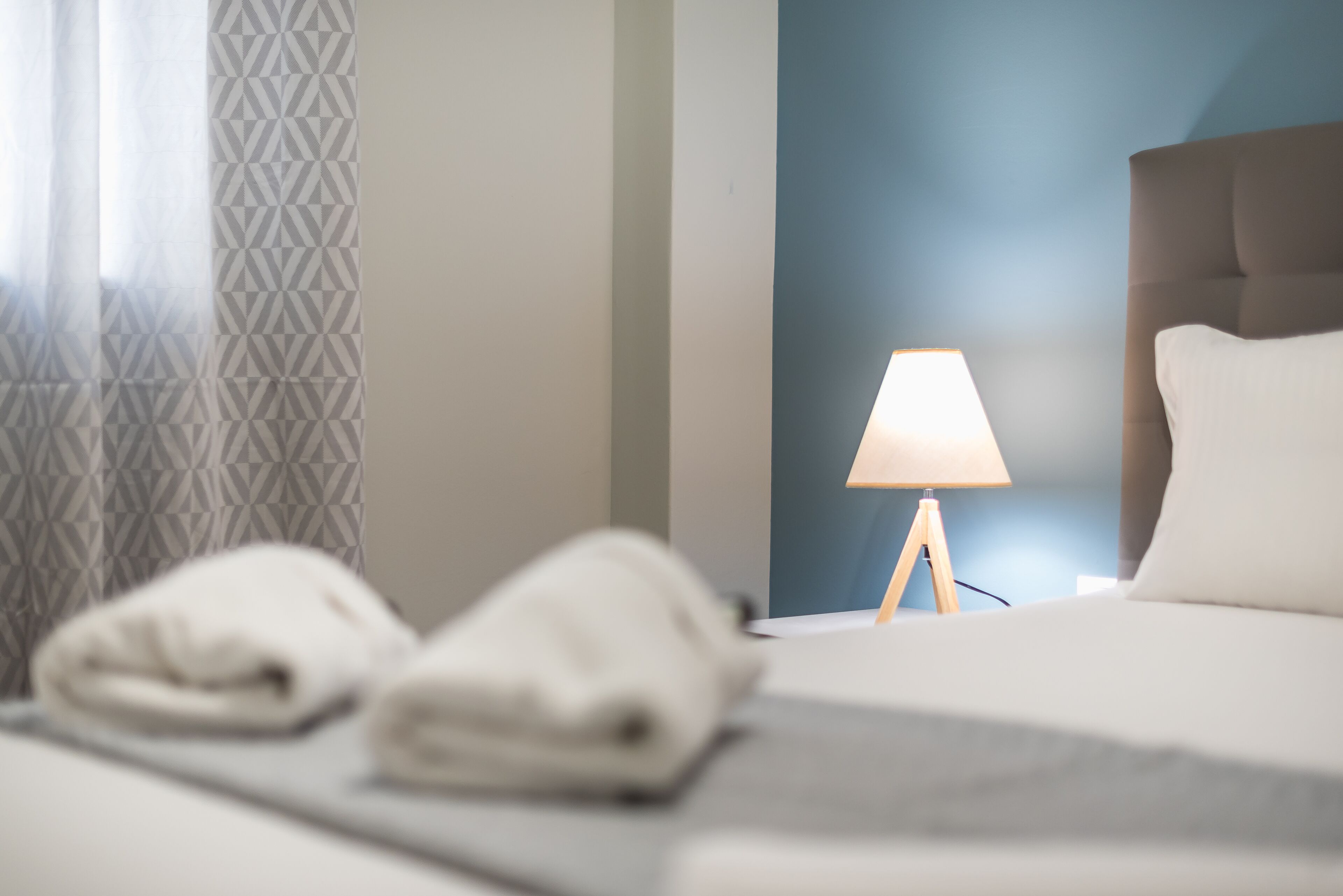 Un lit bien fait, avec deux serviettes, une lampe de chevet et un mur d’accent bleu.