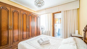 Ett hotellrum med en stor garderob i trä, en säng med vita sängkläder, en kristallkrona och utsikt över omgivningarna genom ett fönster med gardiner.