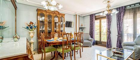 Un comedor con mesa y sillas de madera, un aparador con puertas de vidrio y un televisor en la pared.
