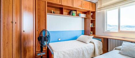 A bedroom with two beds, wooden cabinets, a fan, and a window with a view.