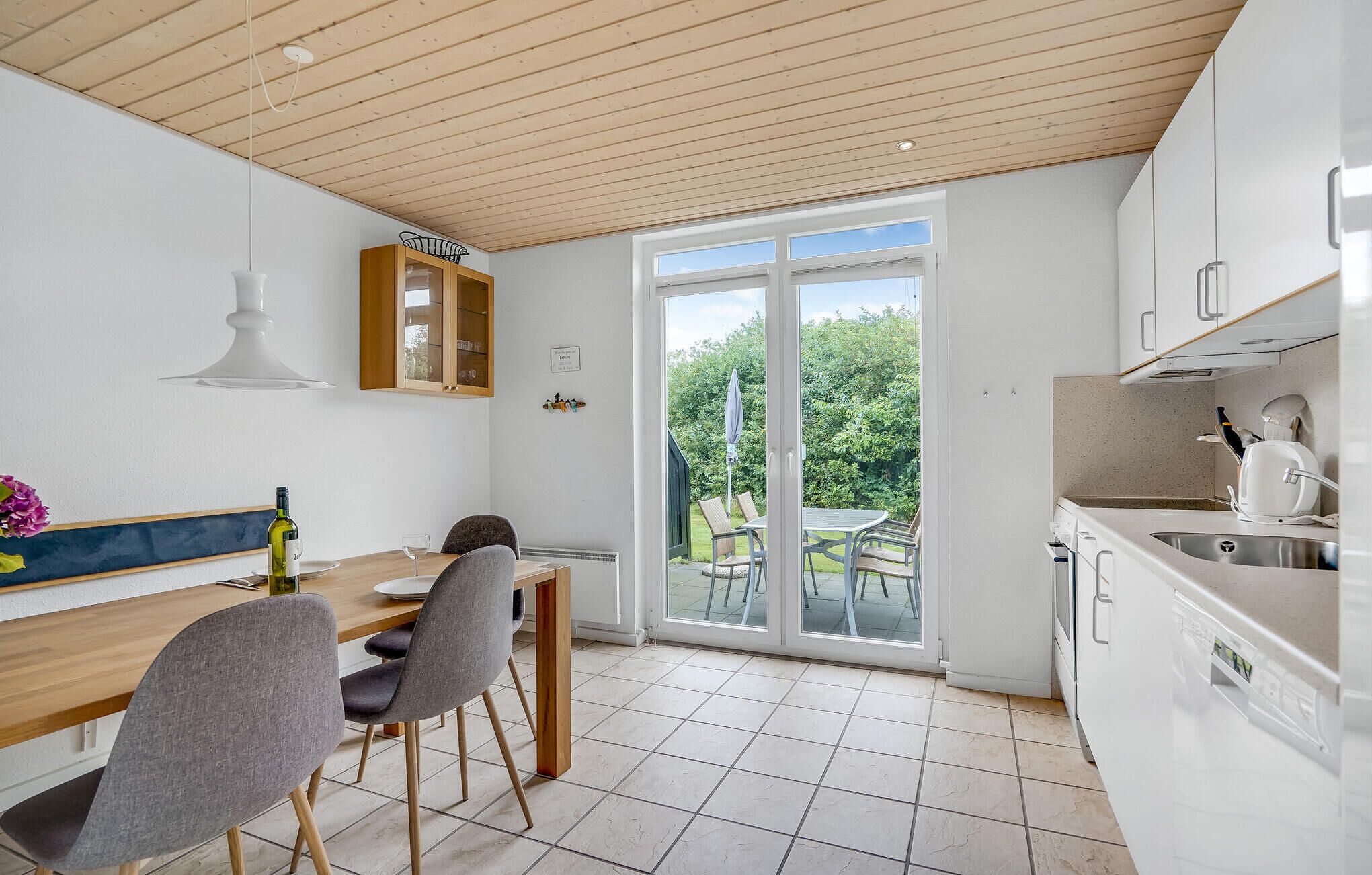 Een moderne keuken met witte kastjes, een houten eettafel en een grote schuifdeur die uitkomt op een tuin.