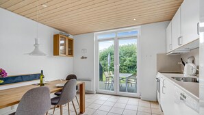 Una cocina moderna con armarios blancos, una mesa de comedor de madera y un amplio ventanal corredero que da a un jardín.
