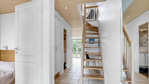 Un interior moderno con una escalera de madera que sube a un dormitorio tipo loft, un baño a la vista y un comedor.