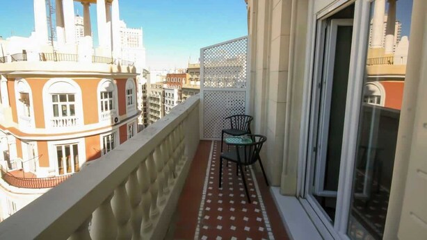A balcony with a chair, a window, and a view of a building with columns. - Gran Vía Terrace w/ Royal Palace Views, Central (Madrid)