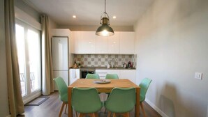 A dining area with a wooden table and four chairs, a kitchen in the background, and a window with curtains. - Gran Vía Terrace w/ Royal Palace Views, Central (Madrid)