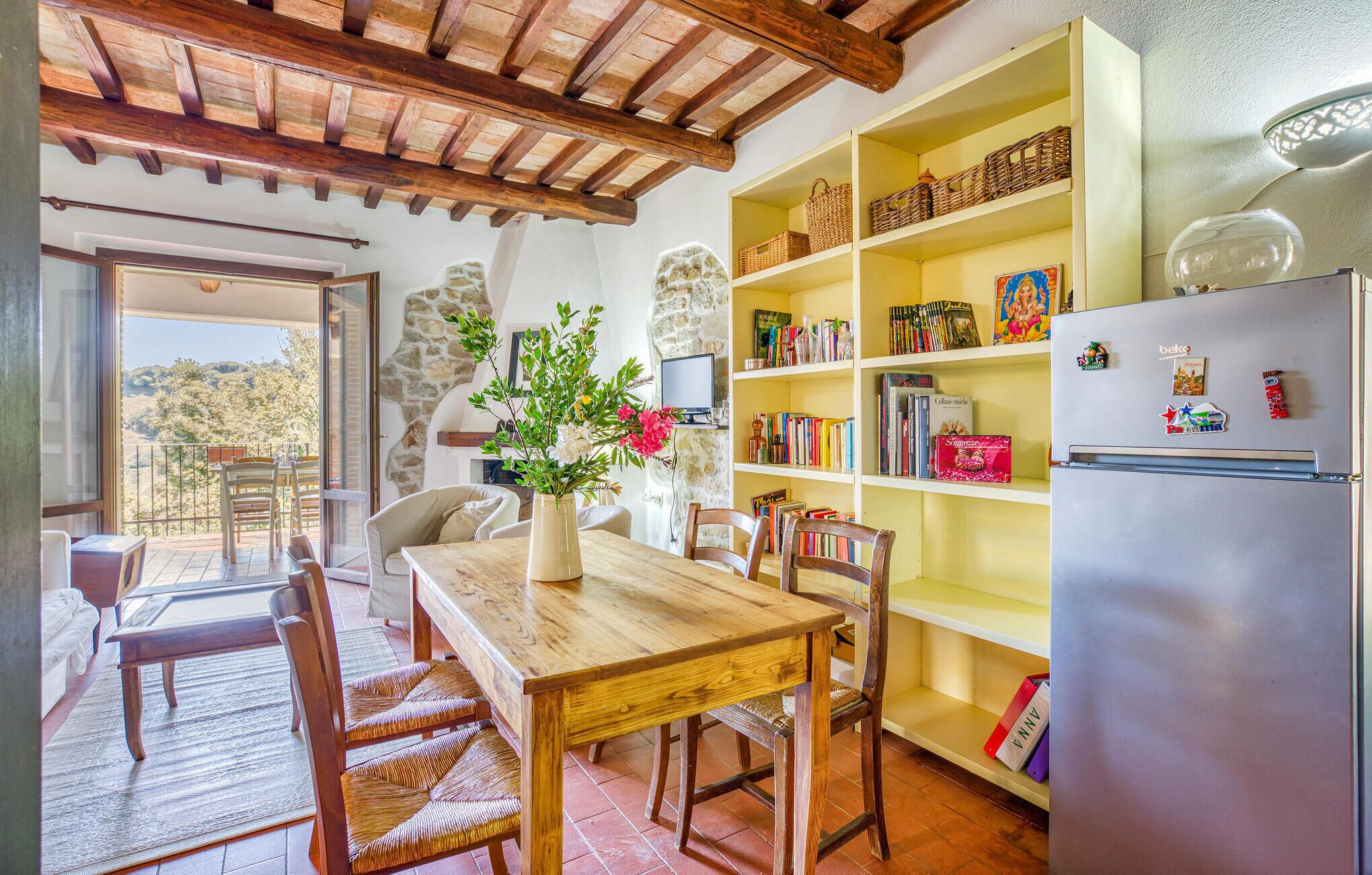 Une cuisine chaleureuse avec une table en bois, des chaises, une bibliothèque et un réfrigérateur.