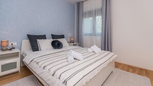 A bedroom with a bed, two bedside tables, a window with curtains, and a wall with a blue pattern. - Cozy apartment in Sukosan with WiFi (Sukosan)