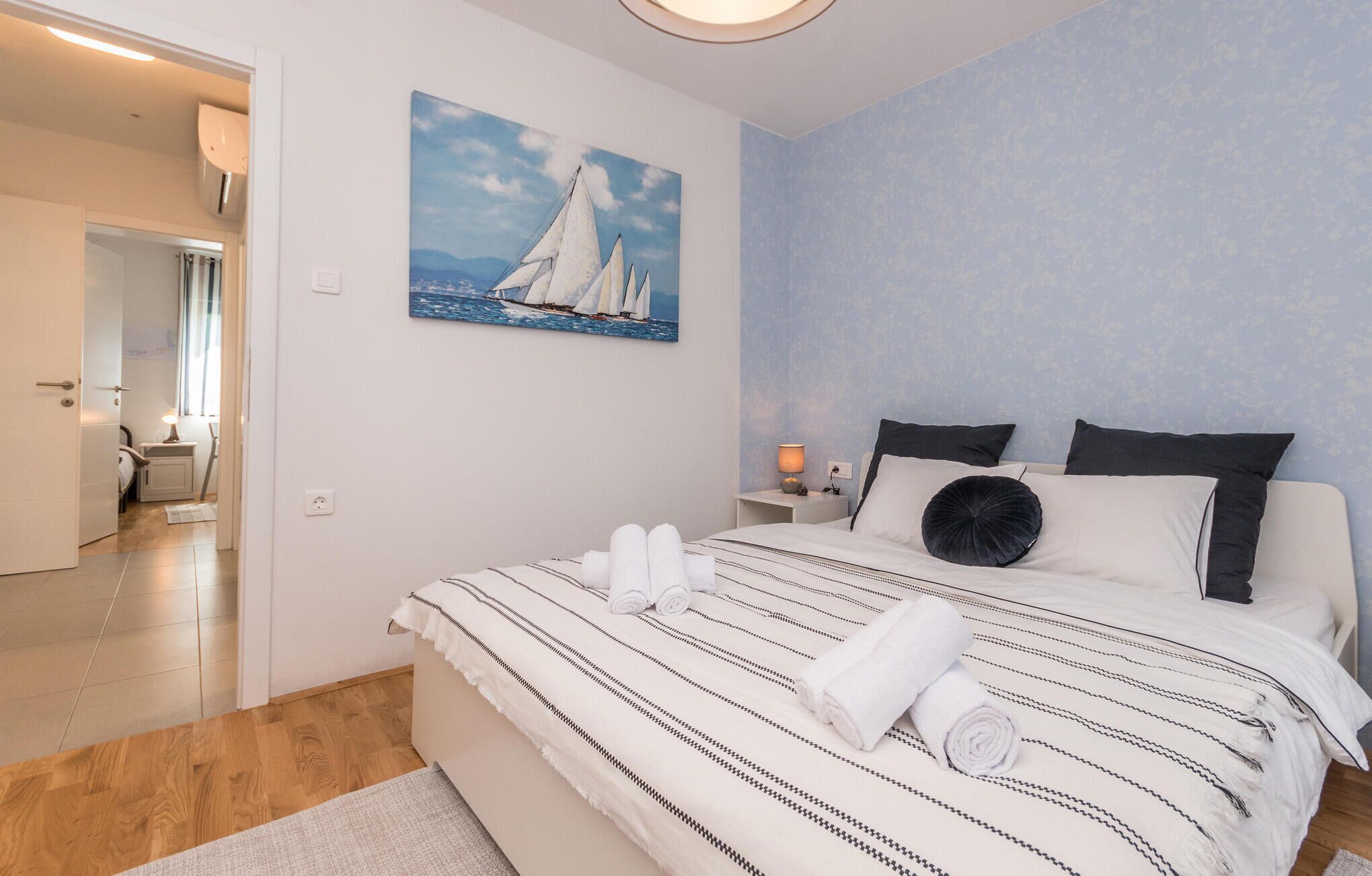 Un dormitorio con una cama, un cuadro de veleros, una mesita de noche y una lámpara.