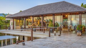 A modern building with a sloped roof, large glass windows, and outdoor seating areas. - In 1 word: WOW! Unique, Breathtaking and Luxury! (Candidasa)