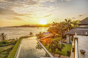 Un resort con piscina, sillones de descanso y vista al océano al atardecer.