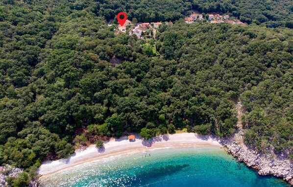 Overlooking a serene beach with turquoise waters and white sand, this property offers a tranquil forested retreat.