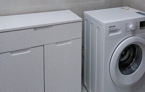Una lavadora blanca con pantalla digital y panel de control, junto a un armario blanco con varios compartimentos.