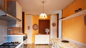 Una cocina compacta con estufa a gas, armarios blancos, una mesa de comedor con sillas, una lámpara colgante y un suelo estampado.