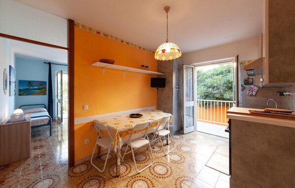 Een compacte keuken met een eethoek, een kleine televisie en een balkon met uitzicht op groen.