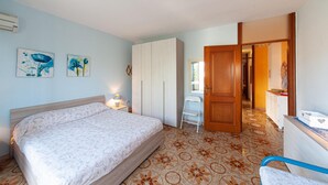 Un dormitorio con cama, mesita de noche, silla, armario y baño visible a través de una puerta abierta.