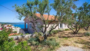 Ein Haus mit rotem Ziegeldach, umgeben von Grünpflanzen und freiem Blick auf das Meer.