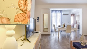 A modern living room with a flat-screen TV, a dining area with a table and chairs, and a kitchen visible through an open doorway. - 2 bedroom awesome apartment in Trappeto (Trappeto)