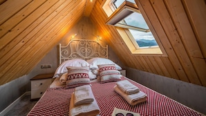 Ein gemütliches Schlafzimmer im Dachgeschoss mit schrägen Wänden, einem Bett mit gemusterten Textilien und einem Dachfenster.