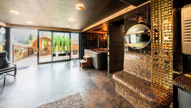 Ein modernes Interieur mit einer großen Glasdoor, die auf eine Außenterrasse führt, einem Sitzbereich mit einer Mosaikwand und einer Küchenzeile inklusive Backofen.