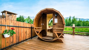 Ein fassförmiger Raum aus Holz mit einer Sitzbank, einem kleinen Tisch und Blick ins Freie.