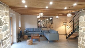 A modern living room with a stone wall, a blue sofa, a wooden coffee table, and a staircase. - House (Neulliac)